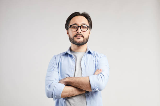 istock Serious confident young Asian web designer with black beard standing against isolated background and looking at camera 1179662341