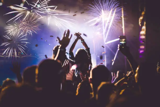 Photo of cheering crowd with raised hands and falling confetti at concert - music festival