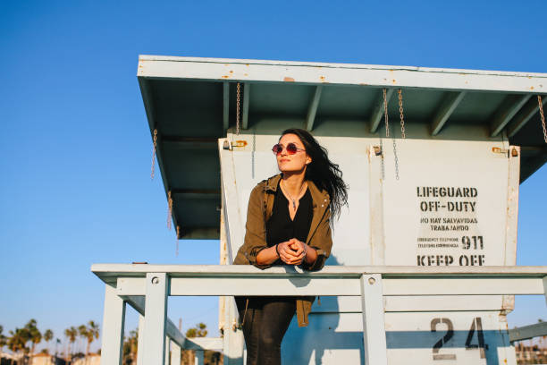 Young woman enjoying the beautiful ocean view from the Venice beach in Los Angeles, California. She is wearing casual clothing, an olive colored jacket, having a relaxed afternoon.