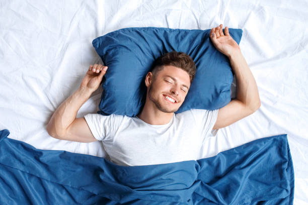 istock Bedtime. Guy lying on bed top view sleeping hands up happy 1179678973