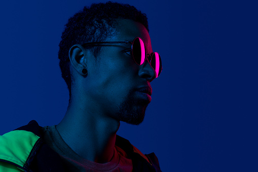 Closeup profile portrait of ethnic black man wearing fashion black sunglasses in blue and pink colors