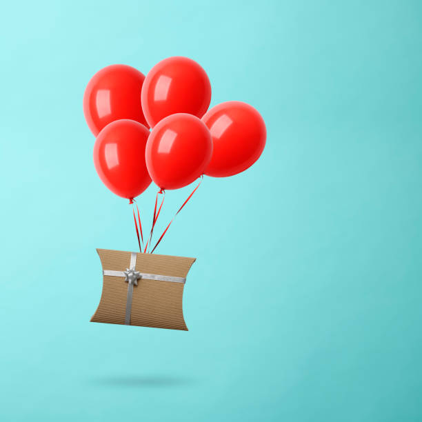 istock Christmas gift box with balloons in mid-air against light blue background 1179689259