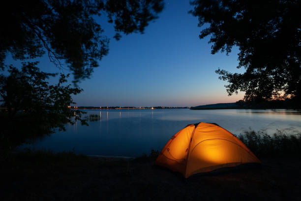 istock Orange illuminated inside tent surrounded by silhouette of tree branches on lake at night 1179696503