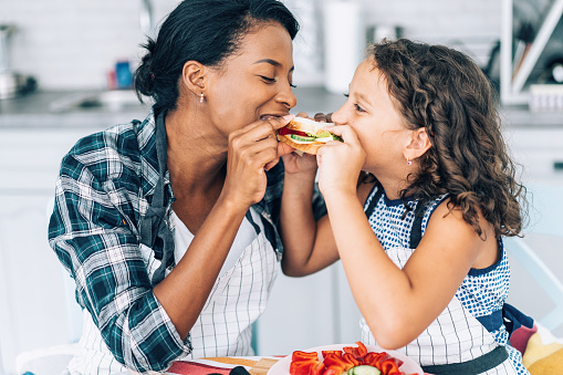 Mixed race mother and daughter eating healthy sandwich with vegetables together in the kitchen