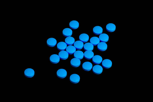Blue pills are scattered on a black background