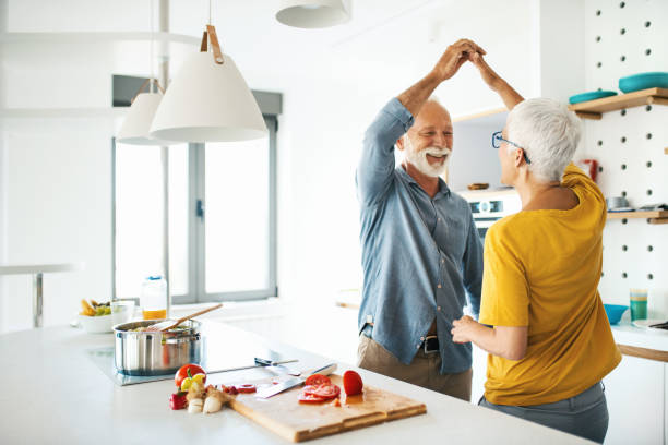Mature couple having fun while cooking lunch. Closeup side view of a mid 60's couple having fun while cooking lunch together. They are dancing next to kitchen counter as the vegetable soup is slowly simmering. middle aged couple dancing stock pictures, royalty-free photos & images