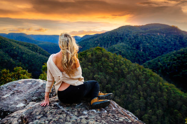 istock Woman sitting on high rock overlooking valleys as sun sets 1179718216