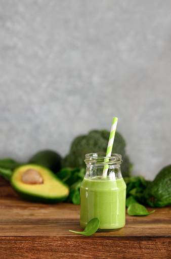 Green detox smoothies made of spinach and avocado in a glass bottle with a straw, front view