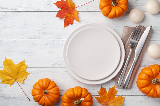 Autumn Thanksgiving table setting for dinner with plate, knife, fork decorated pumpkins and maple leaves. Top view with copy space.