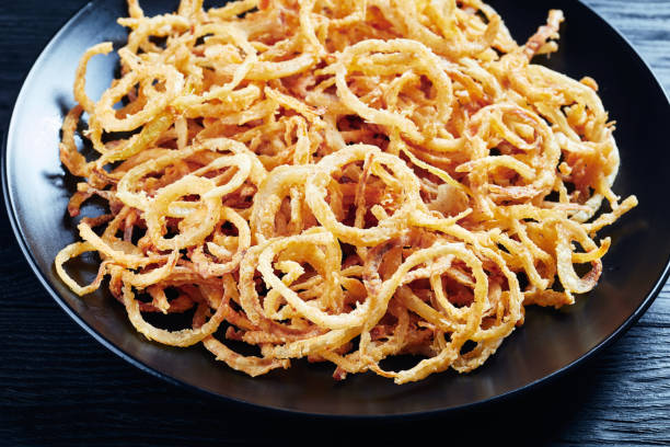 french crispy fried onions on a black plate on a wooden table close-up of french crispy fried onions on a black plate on a wooden table, horizontal view from above, crunchy stock pictures, royalty-free photos & images