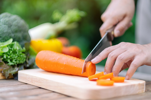 Closeup image of a woman cutting and chopping carrot by knife on wooden board
