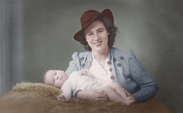 ritratto vintage retrò del 1943 di colore digitale di una giovane madre con cappello fedora e il suo bambino che guarda e sorride alla macchina fotografica - 1940s style foto e immagini stock