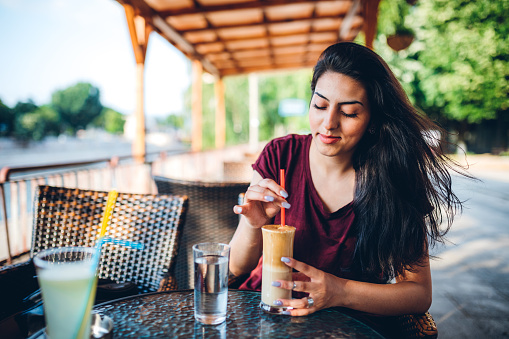 Beautiful gypsy young woman in cafe drinking ice coffee.