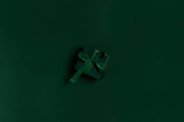 Green gift box with green ribbon on green background, copy space