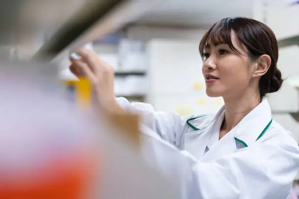 Young chemist arranging medicines on shelf. Female pharmacist is working in pharmacy. She is standing in medical store.