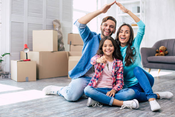 We’re in the house! Mom and dad are imitating a roof of the house with their hands while their daughter holds keys from their new apartment in her hands. House moving concept. stock photo