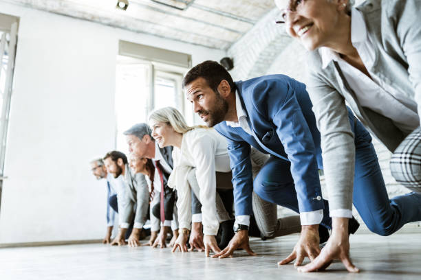 Ready, set, go! Large group of business people on a starting line ready for sports race in the office. Focus is on man in blue suit. Copy space. office competition stock pictures, royalty-free photos & images