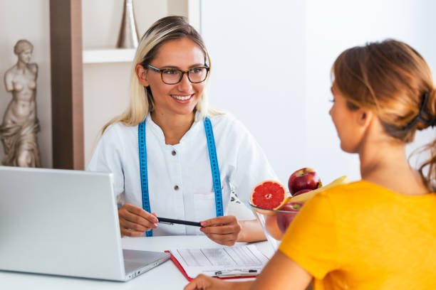 porträt einer jungen lächelnden ernährungsberaterin im sprechzimmer. diät-plan. junge frau zu besuch ernährungsberaterin in gewichtsverlust klinik - document healthcare and medicine stethoscope history stock-fotos und bilder