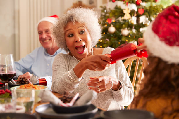 grand-mère tirant le craquelin de noel avec la petite-fille pendant qu'ils s'asseyent pour le repas à la table - christmas cracker photos et images de collection