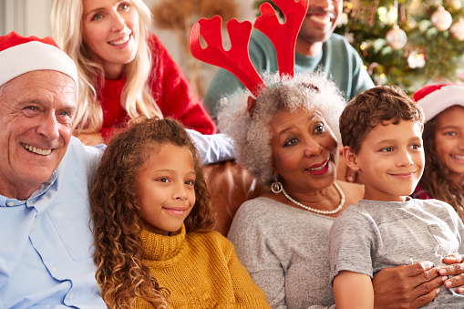 Multi-Generation Family Sitting On Sofa At Christmas Watching Television Together