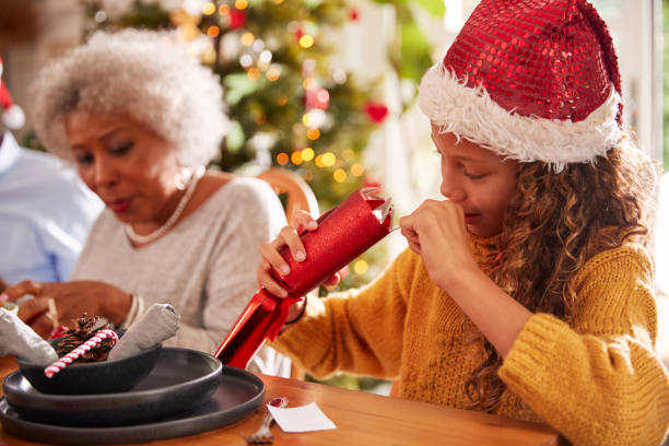 grand-mère tirant le craquelin de noel avec la petite-fille pendant qu'ils s'asseyent pour le repas à la table - pulling a name from a hat photos et images de collection