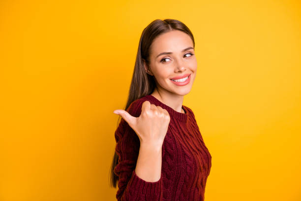istock Portrait of lovely lady pointing at copy space showing ads wearing maroon pullover isolated over yellow background 1179751366