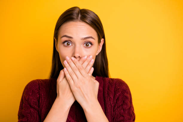 Close up photo of girl with her mouth covered with hands while isolated with yellow background keeping silence Close up photo of girl with her mouth, covered with hands while isolated with yellow background keeping silence closed mouth stock pictures, royalty-free photos & images