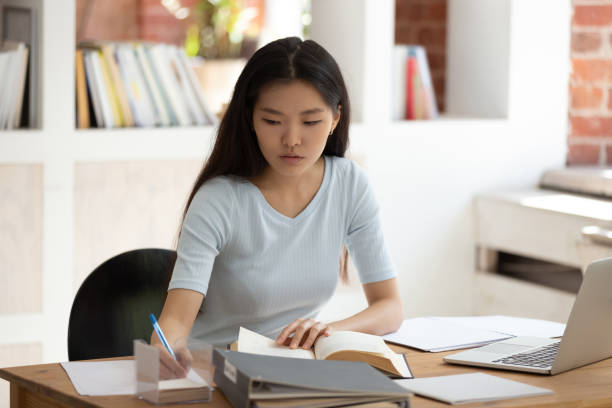 istock Concentrated young Asian female student sitting at desk in library. 1179756315