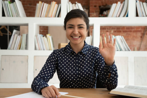 Happy indian female student waving hello at camera.