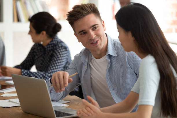 istock Handsome caucasian young guy helping asian female groupmate with abstract. 1179756345