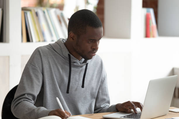istock Serious black male student using laptop, busy with studying. 1179756383