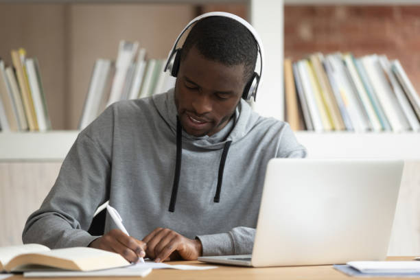 istock Focused black student wearing bluetooth earphones, busy with study, 1179756389