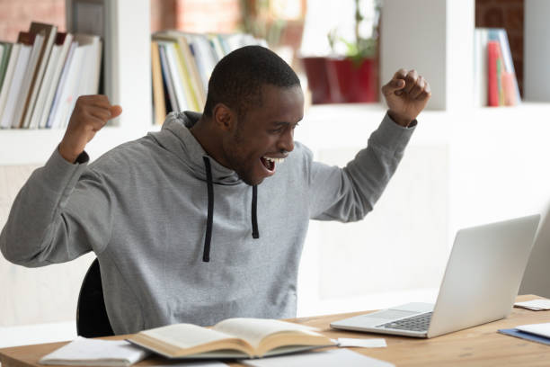 jeune étudiant masculin américain africain surjoué célébrant de bons résultats d'examen. - résultat dexamen photos et images de collection