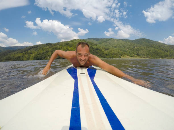 Young man paddles on a long-board in lake. He is having fun.