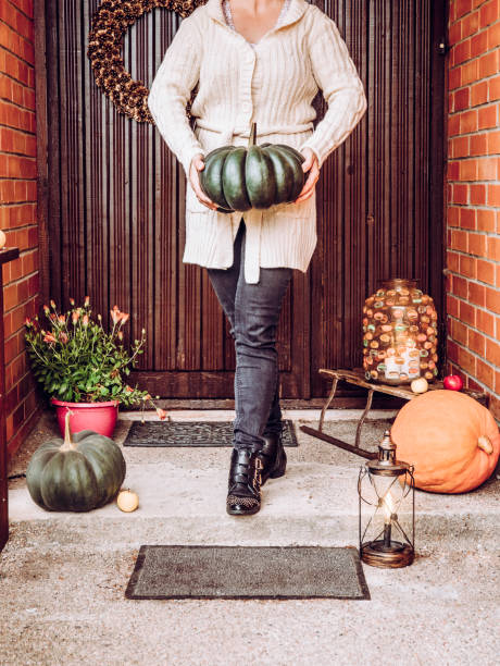 戸口に立つ正体不明の女性は、居心地の良い白いニットのセーターを着て、緑のマスカットカボチャを手に持っている。アウトドアシーズンのエクステリアホーム秋の装飾コンセプト。 - single flower flower autumn pumpkin ストックフォトと画像