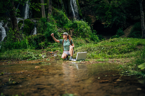 One woman, lady explorer and biologist taking a water sample in nature by waterfall alone.