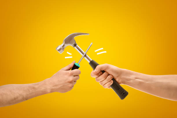 istock Hand holding screwdriver fighting with hand holding hammer on yellow background 1179758667