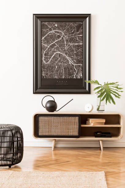 istock Modern scandinavian living room interior with black mock up poster map frame, design commode, water can, tropical leaf, books and elegant accessories. Template. Stylish home decor. White walls. 1179759965