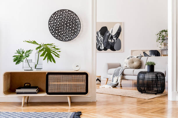 istock Scandinavian and design home interior of open space with wooden commode, gray sofa, design black rattan decoration, tropical leafs and elegant personal accessories. Stylish art home decor. Template. 1179760036