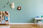 Interior design of scandinavian childroom with wooden cabinet, mint armchair, white desk, a lot of plush and wooden toys. Eucalyptus color of background walls. Plush animal head on the wall. Template