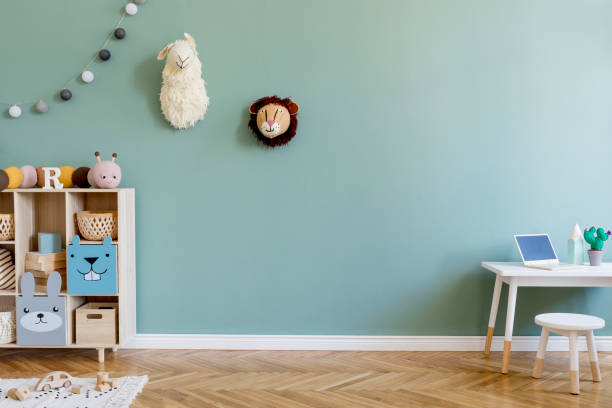 Interior design of scandinavian childroom with wooden cabinet, mint armchair, white desk, a lot of plush and wooden toys. Eucalyptus color of background walls. Plush animal head on the wall. Template Stylish scandinavian kid room. Design interior of childroom. Template Home decor concept. kid goat stock pictures, royalty-free photos & images