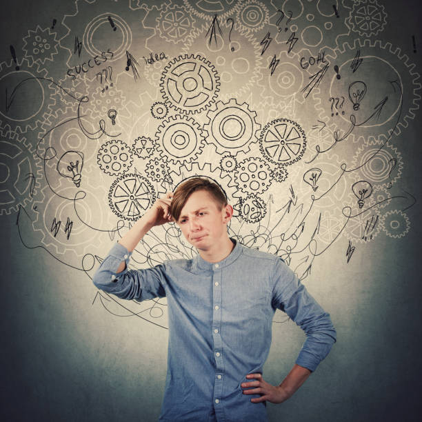 istock Pensive teenage boy scratching his head looking confused has questions. Perplexed guy thinking of new ideas as gear cogwheels, arrows and mess sketch as thoughts around head. Find solution to problem. 1179761455