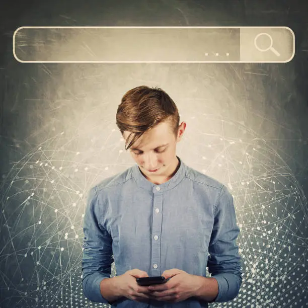 Photo of Curious teenager boy using his mobile phone browsing network search bar to find useful information and data. Internet searching engines, modern technology, virtual life and networking concept.