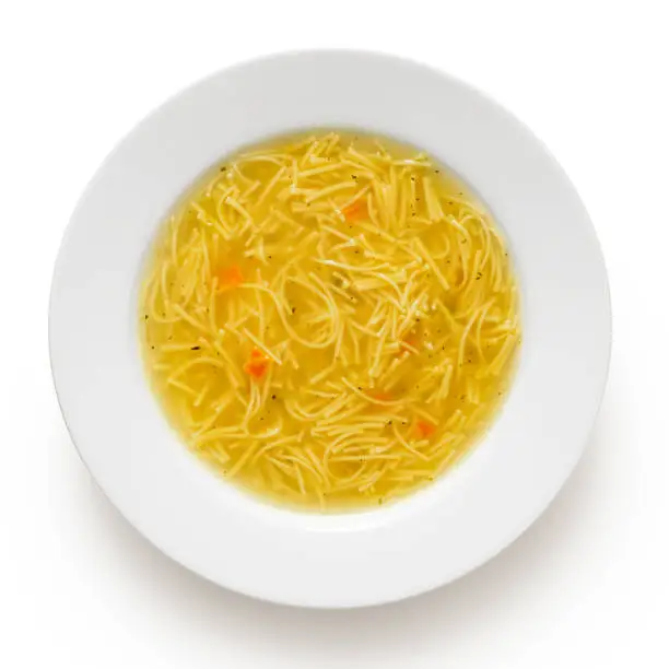 Instant chicken noodle soup in a white ceramic soup plate isolated on white. Top view.