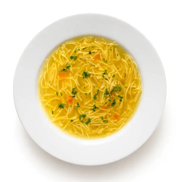 Instant chicken noodle soup in a white ceramic soup plate isolated on white. Top view. Chopped parsley.