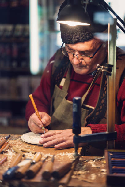 Carpenter carving wooden decorative figurine Close-up image of senior artist working on decorative wooden plate carpenter carpentry craftsperson carving stock pictures, royalty-free photos & images