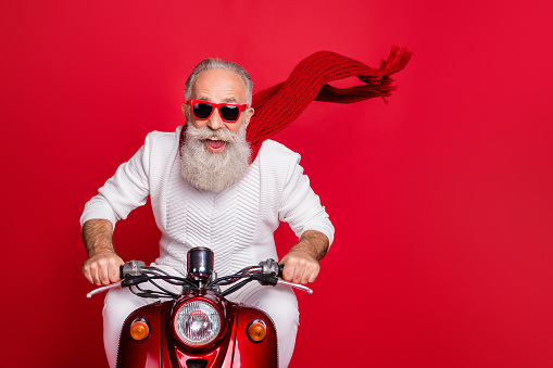 Portrait of elderly modern person in eyewear eyeglasses driving his bike wearing, white sweater isolated over red background