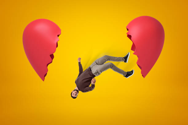 istock Young man in casual clothes falling between two broken heart pieces on yellow background 1179766405