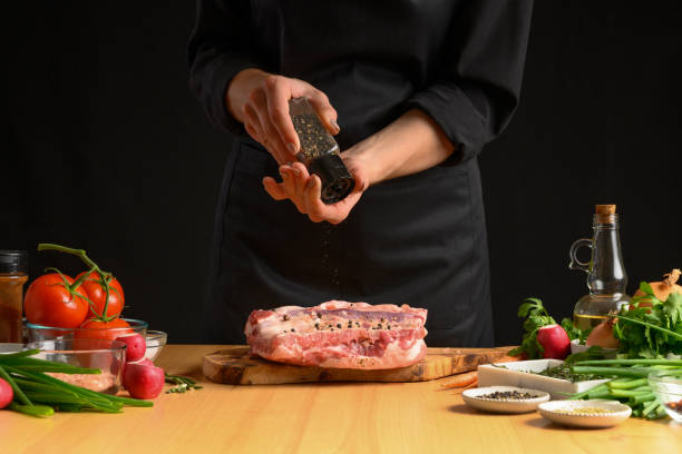istock Chef cooks pork ribs. sprinkling with pepper on a background with vegetables. Freezing in motion. Recipe book, cooking, restaurant business 1179767834