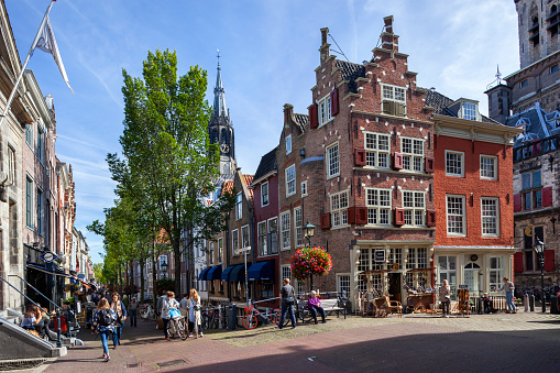 Delft, Netherlands - September 20, 2019: Idyllic view at the corner of Markt and Voldersgracht with people walking and sitting in the sun near historic buildings